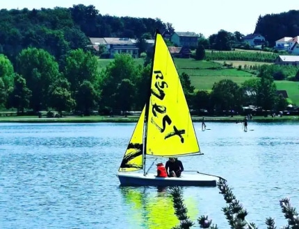 Segelboot auf einem See mit Wald im Hintergrund